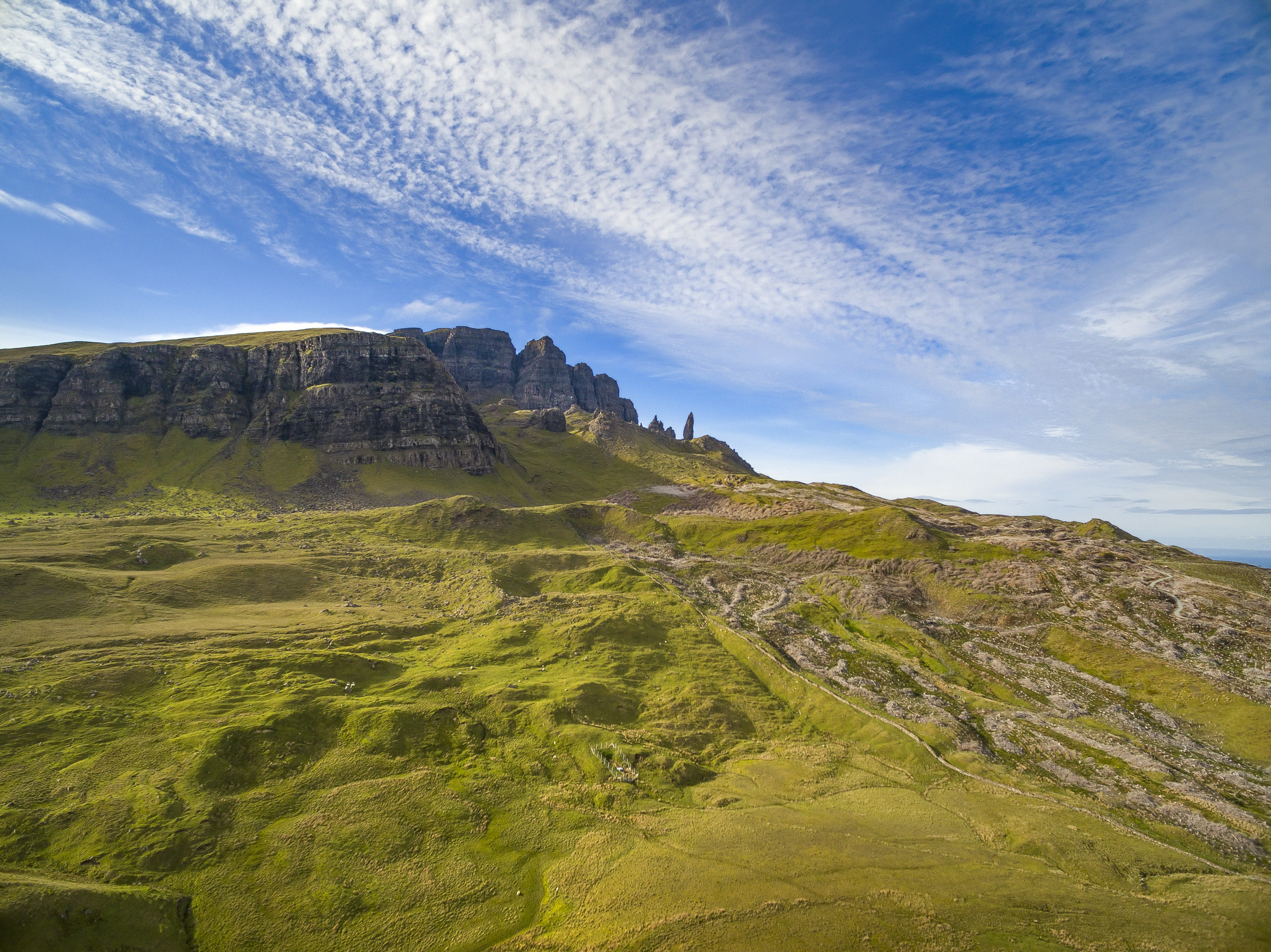 A dramatic photo of the iconic Old Man of Storr, a towering rock pinnacle on the Isle of Skye, Scotland, standing sentinel amidst a rugged landscape of hills, valleys, and misty mountains.