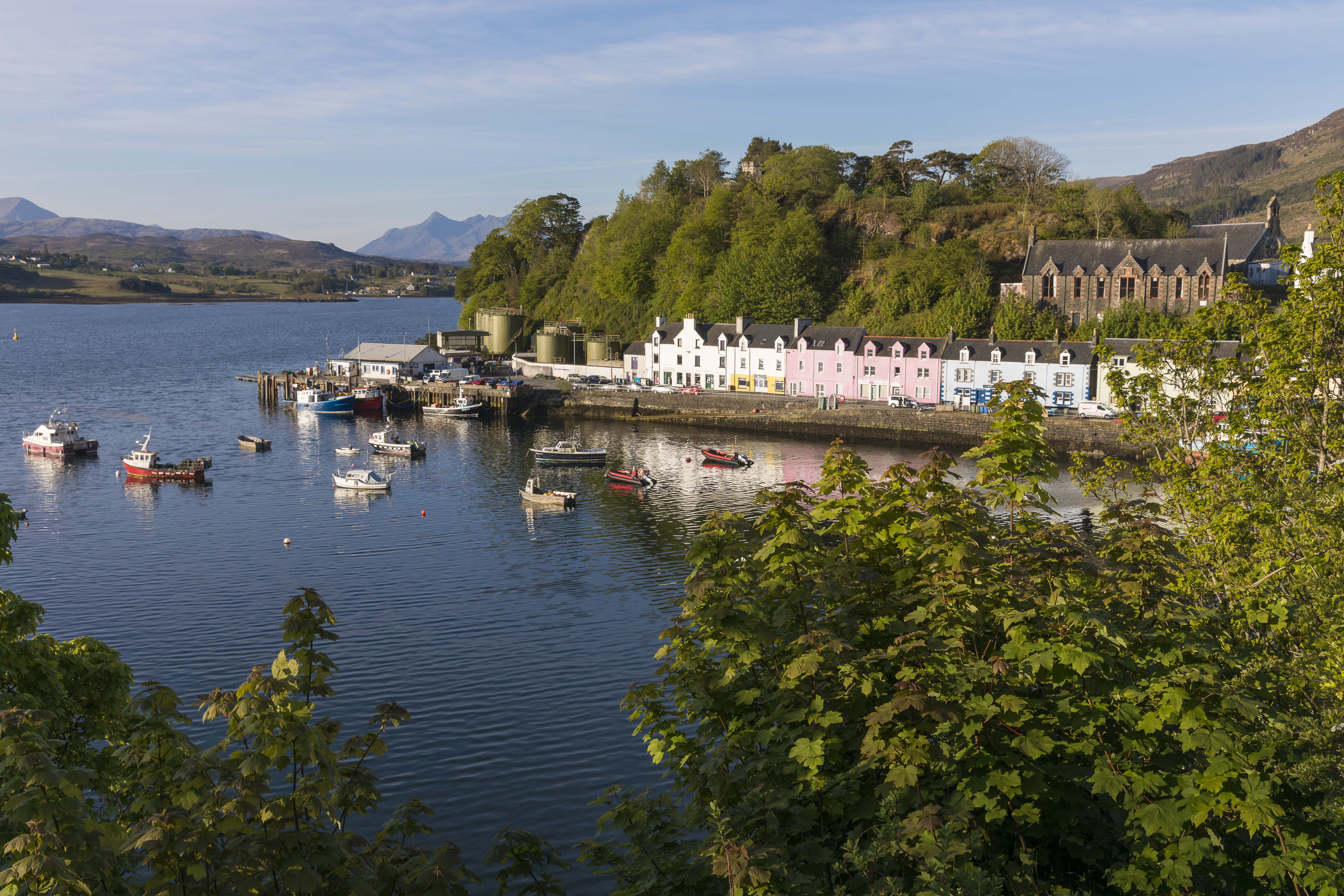 Colorful waterfront houses and boats in Portree, a charming fishing village on the Isle of Skye, Scotland, surrounded by rugged hills and scenic harbor views. 