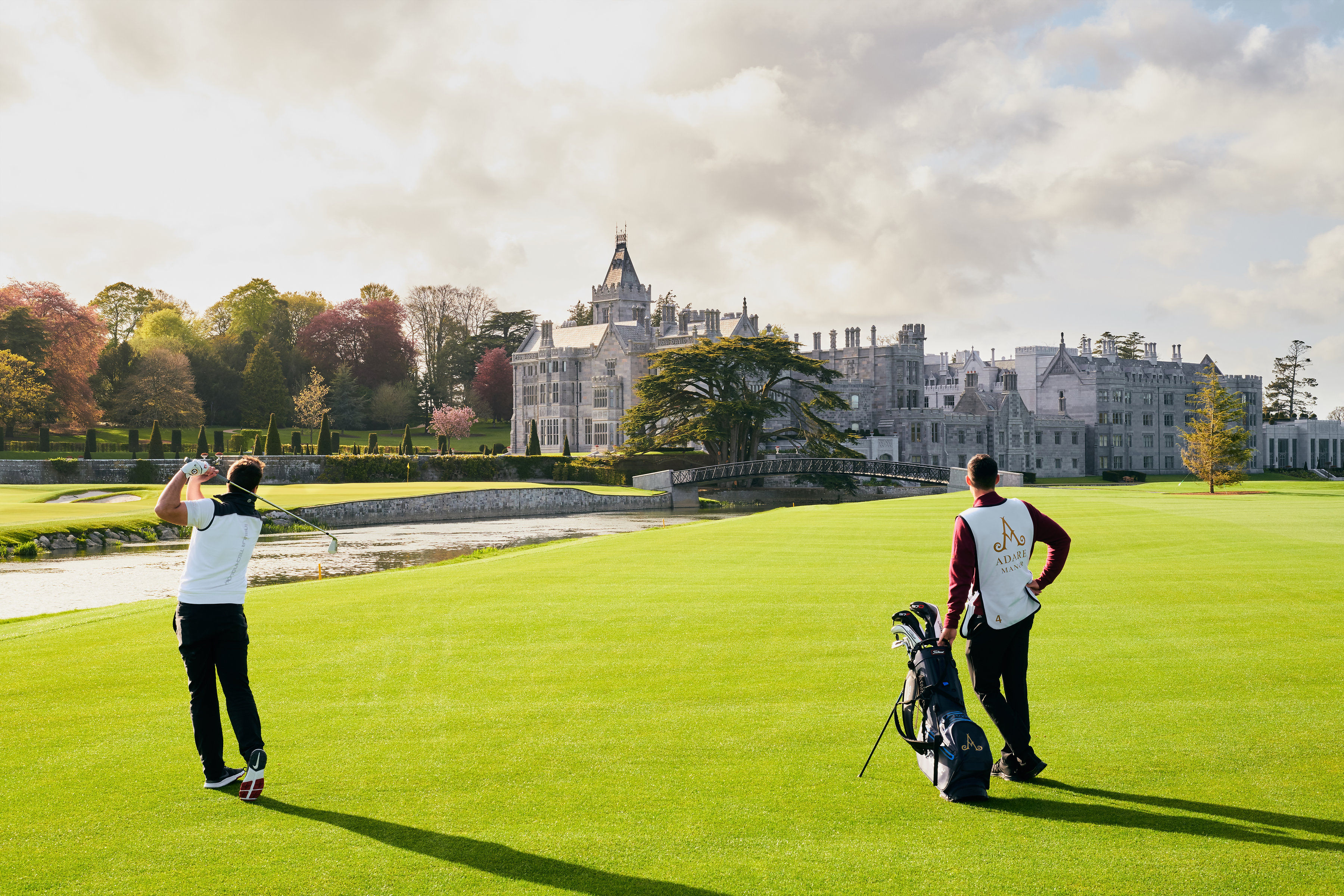 A serene photo of the Adare Manor Golf Course in County Limerick, Ireland, showcasing its immaculately manicured greens, rolling hills, and picturesque surroundings, with the majestic Adare Manor estate visible in the background.