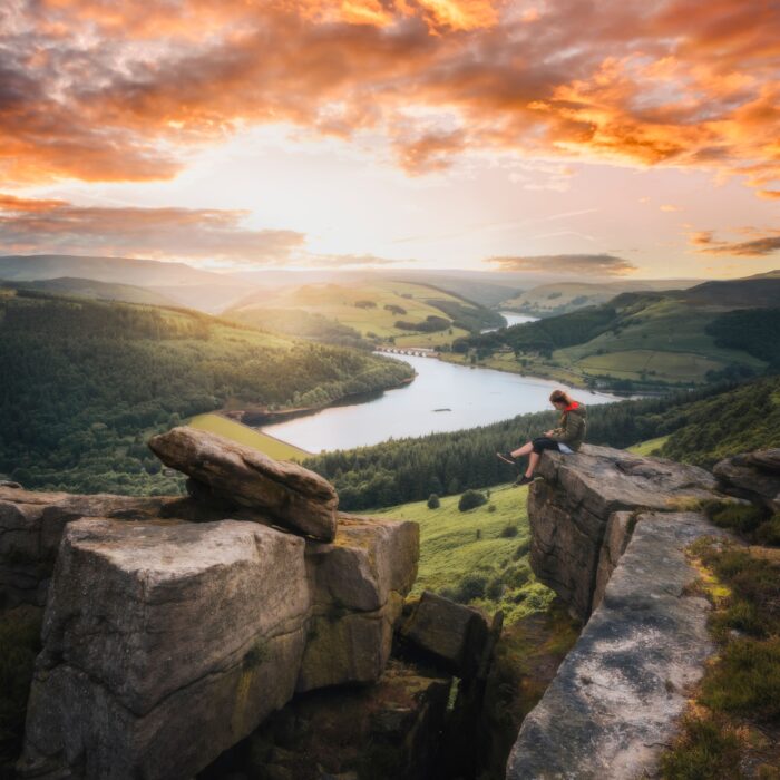 Woman sitting on a rock at Bamford Edge looking down the valley with sunsetting, Derbyshire, England