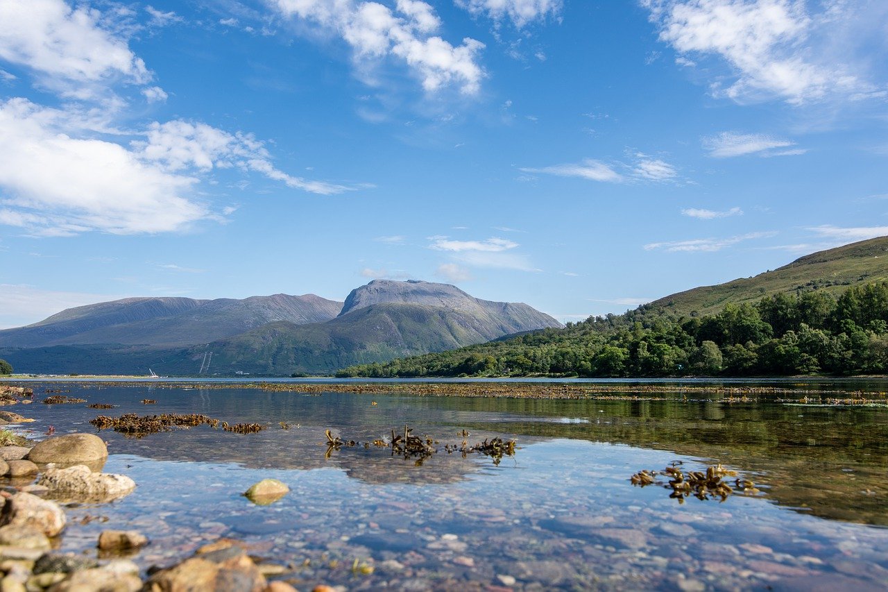 Ben Nevis, the highest mountain in the British Isles, towers above the Scottish Highlands, with a serene loch in the foreground. 