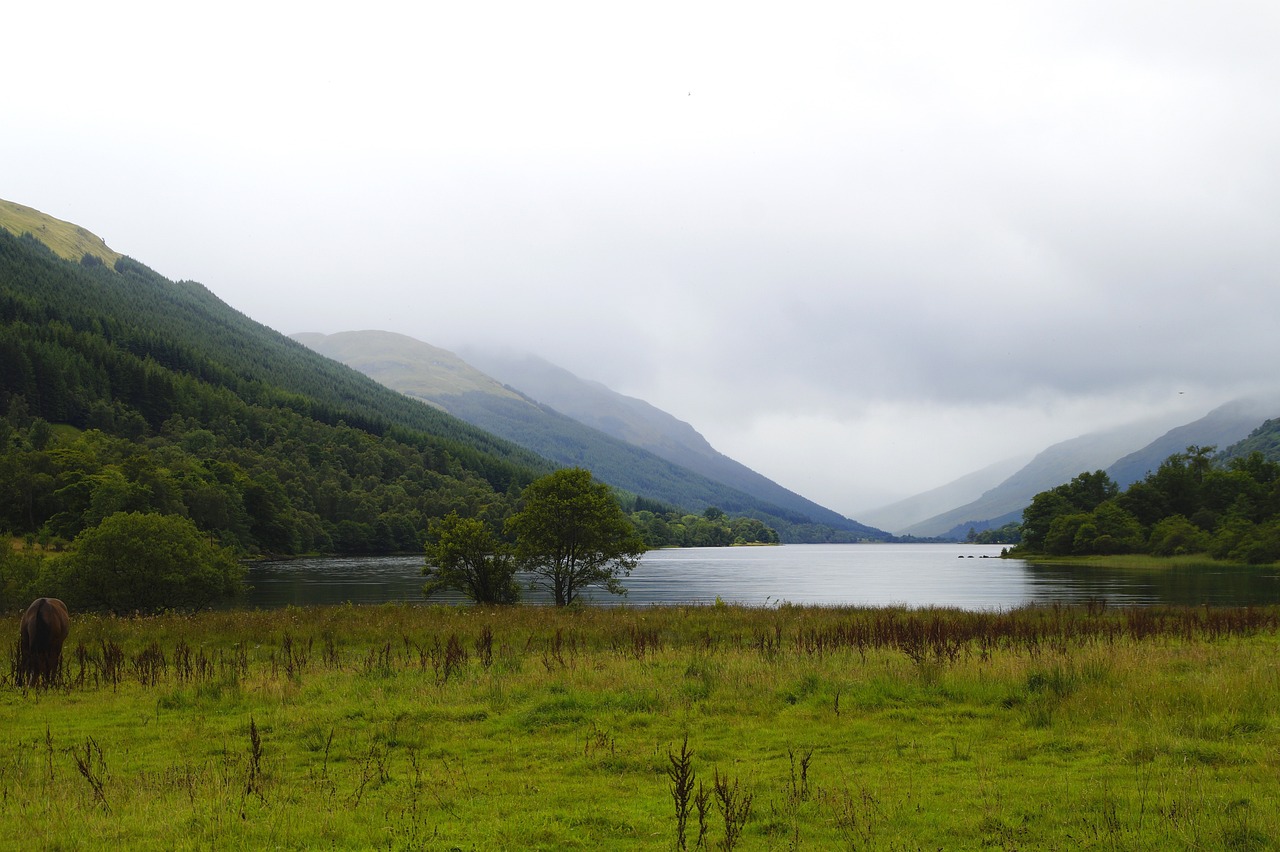 Loch Lomond, Scotland's largest freshwater lake, sparkles in the sunlight, surrounded by rolling hills and towering mountains, with a few boats dotted on its tranquil surface. 