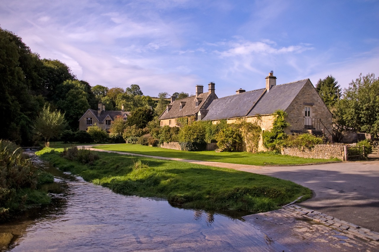 Quintessential Cotswolds village scene, showcasing picturesque stone cottages, rolling hills and lush green landscapes in south-central England.