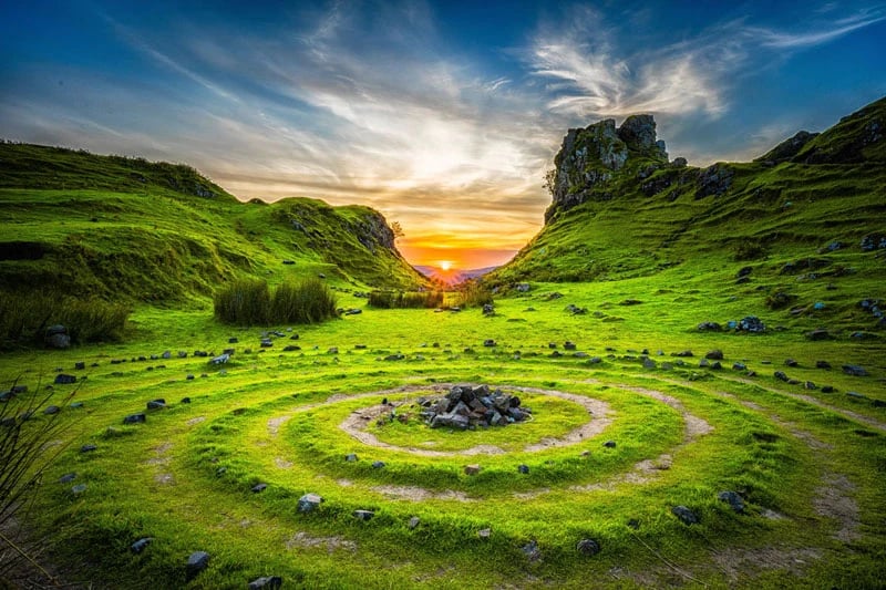 The Fairy Glen on the Isle of Skye, featuring rolling grassy hills, unique rock formations, and winding natural terraces under a soft, cloudy sky.