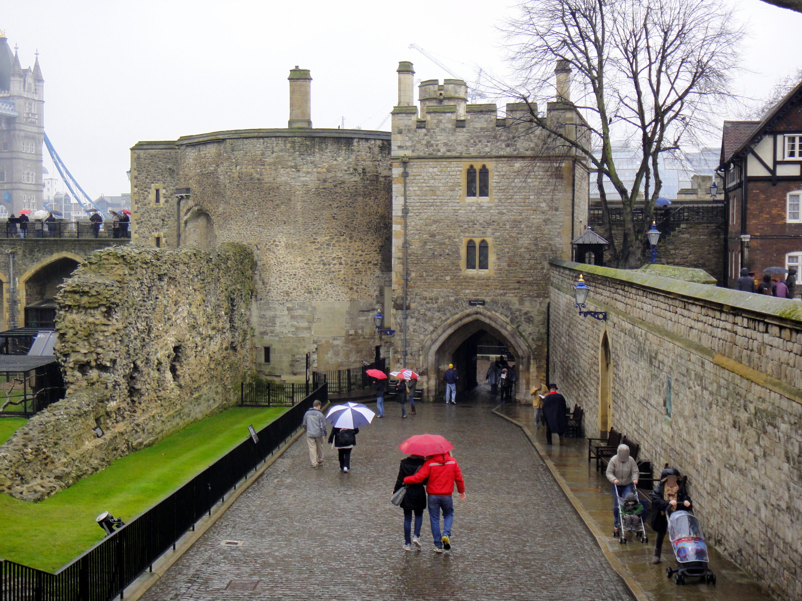 Wakefield Tower (left) and Bloody Tower (right), two medieval stone towers within the Tower of London, are pictured against a cloudy sky, with the castle's battlements and walls visible in the foreground.