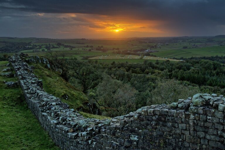 Hadrian's Wall at sunset with vibrant orange and pink hues illuminating the ancient Roman fortification, set against a serene countryside backdrop.